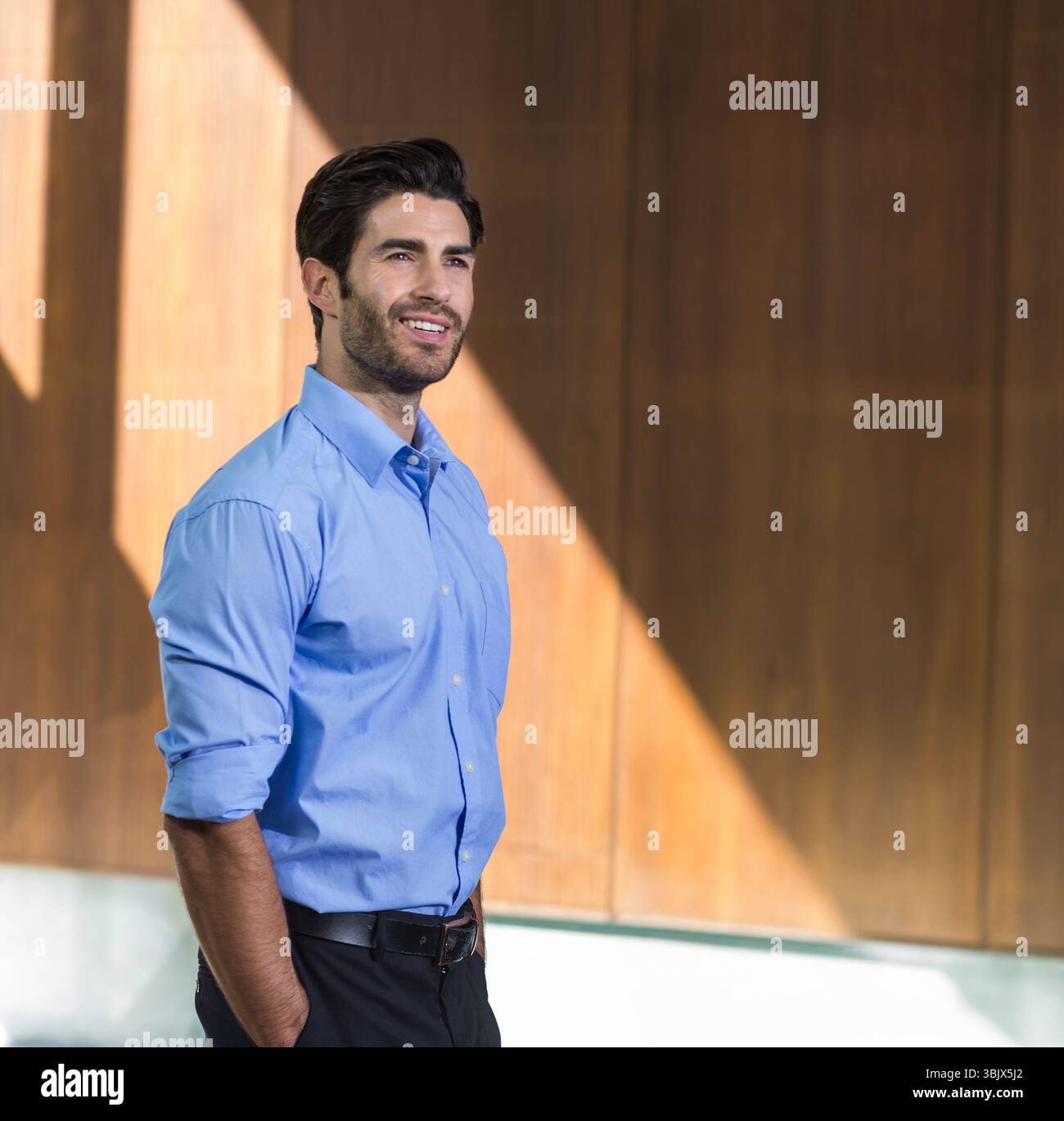 Uomo in piedi nella hall accanto a un pannello di legno che indossa cintura di pelle nera, camicia con bottoni, spazio per le copie Foto Stock
