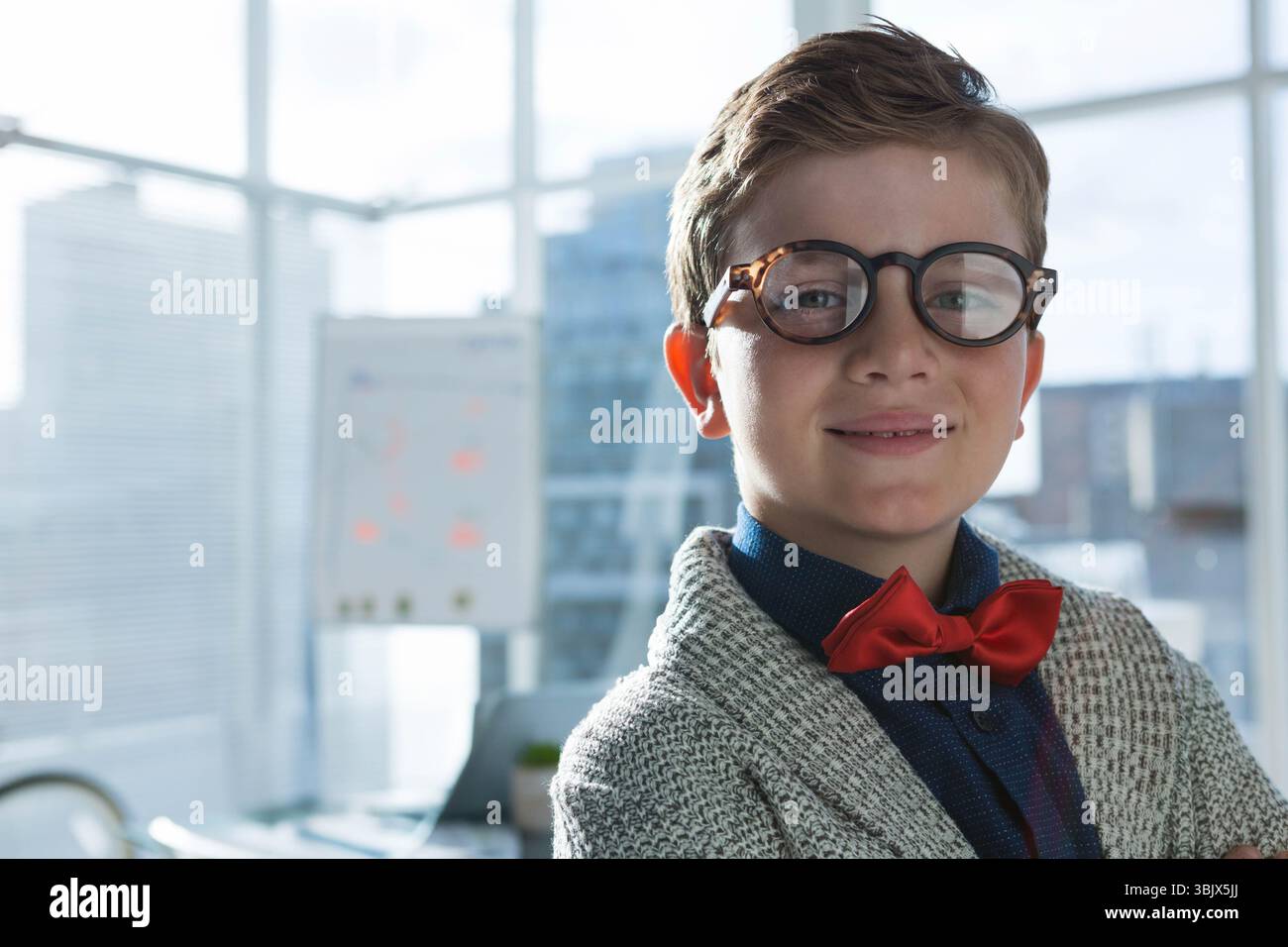 Ragazzo che indossa occhiali rotondi, cravatta rossa, in piedi in ufficio accanto alla lavagna, al laptop, all'impianto, all'area di copia Foto Stock