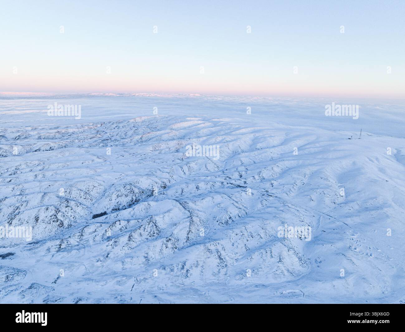 Un'ampia vista aerea di un paesaggio incontaminato e ondulato di tundra innevata sotto un cielo limpido Foto Stock