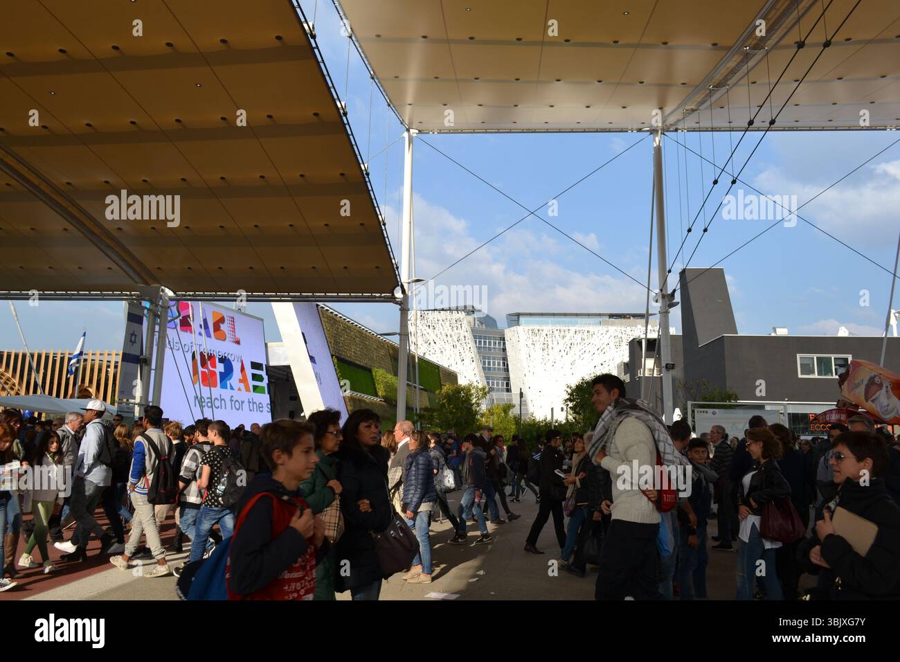 I visitatori della grande mostra camminano lungo la strada principale di Decumano. Padiglioni Italia, Israele, Francia visibili da sotto gli ombrelloni. Interesse, intrattenimento. Foto Stock