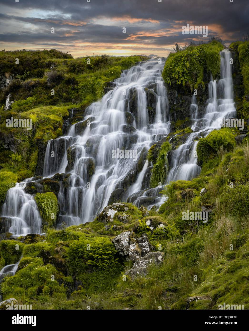 Lussureggiante paesaggio verde caratterizzato da una dolce cascata che scorre giù dalle terrazze rocciose al tramonto. Foto Stock