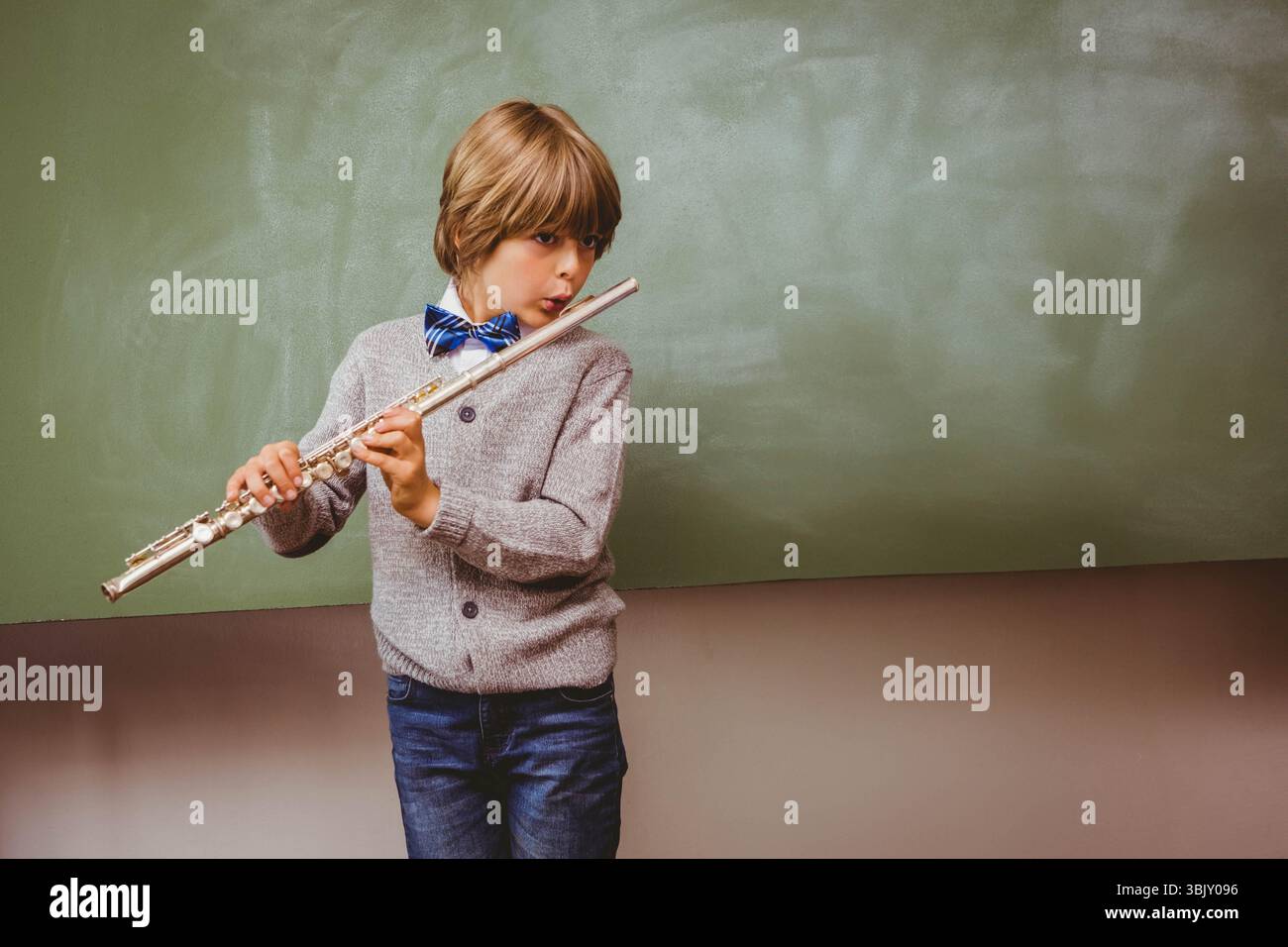 Ragazzo di scuola che gioca a flauto d'argento davanti alla lavagna verde che indossa il cardigan, copia spazio Foto Stock