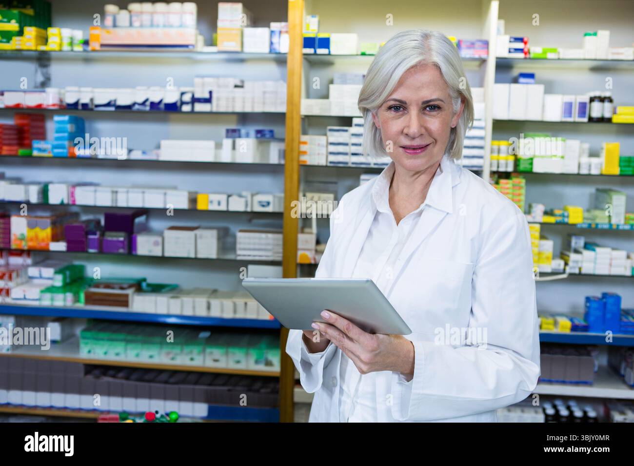 Farmacista donna anziana in possesso di una compressa che organizza i farmaci sugli scaffali della farmacia, copia dello spazio Foto Stock