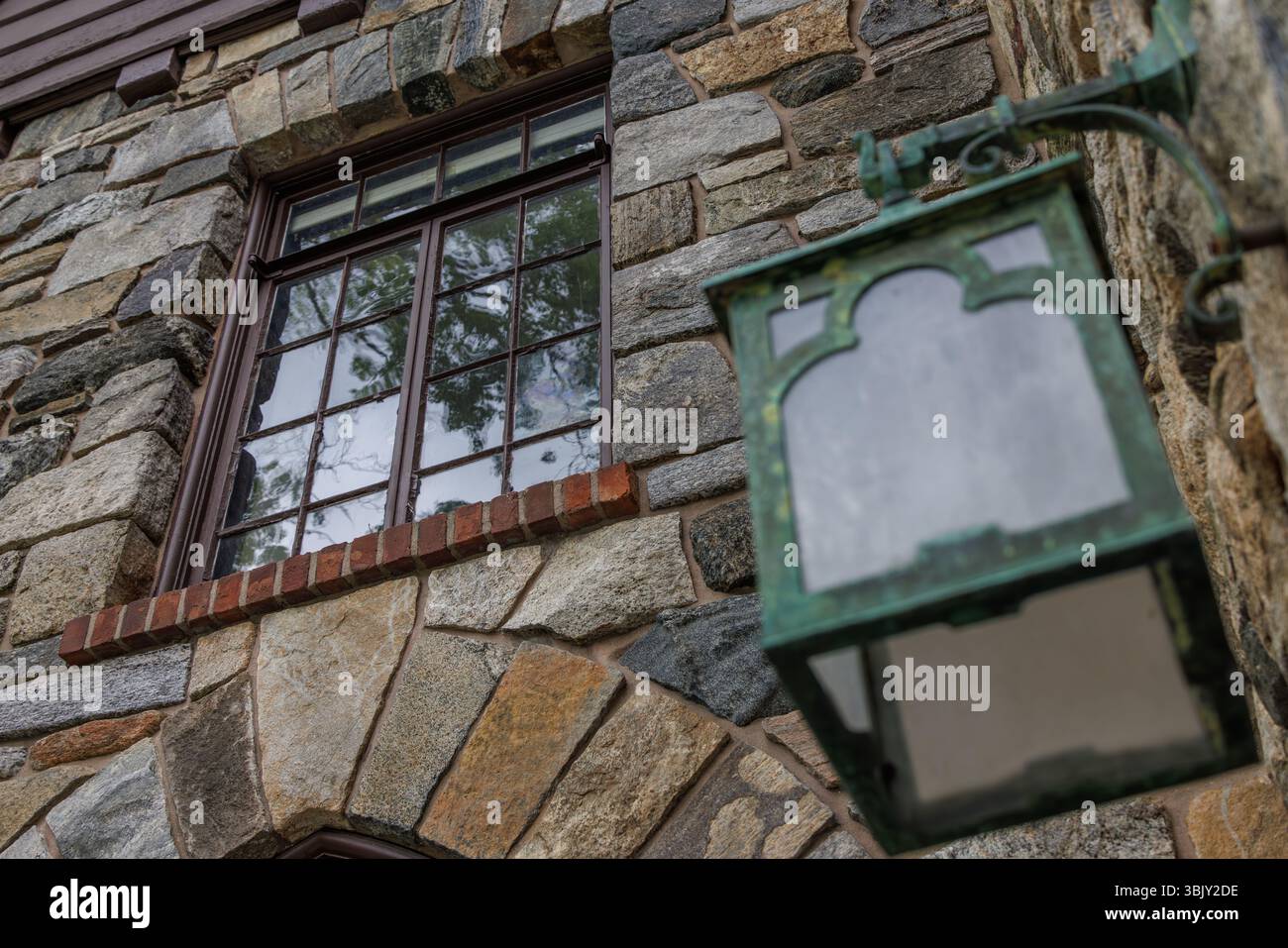 Parete in pietra con finestra rustica e lanterna verde vintage, foto a colori che mostrano texture, riflessi e architettura antica con luce naturale. Foto Stock