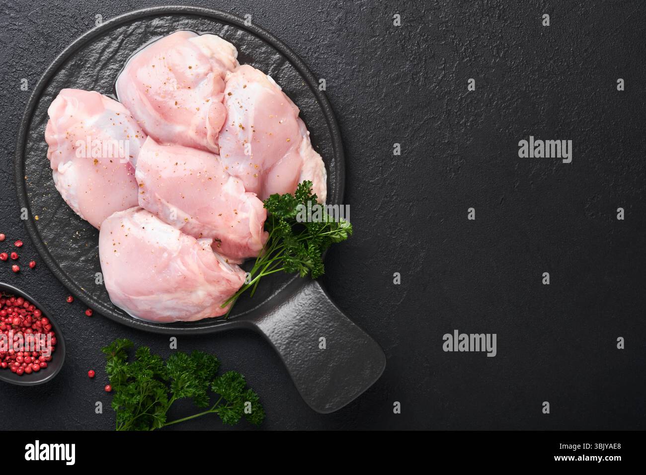 Filetto di coscia di pollo crudo senza pelle con erbe e spezie su sfondo nero. Carni di pollame da allevamento. Vista superiore con spazio di copia. Mo Foto Stock
