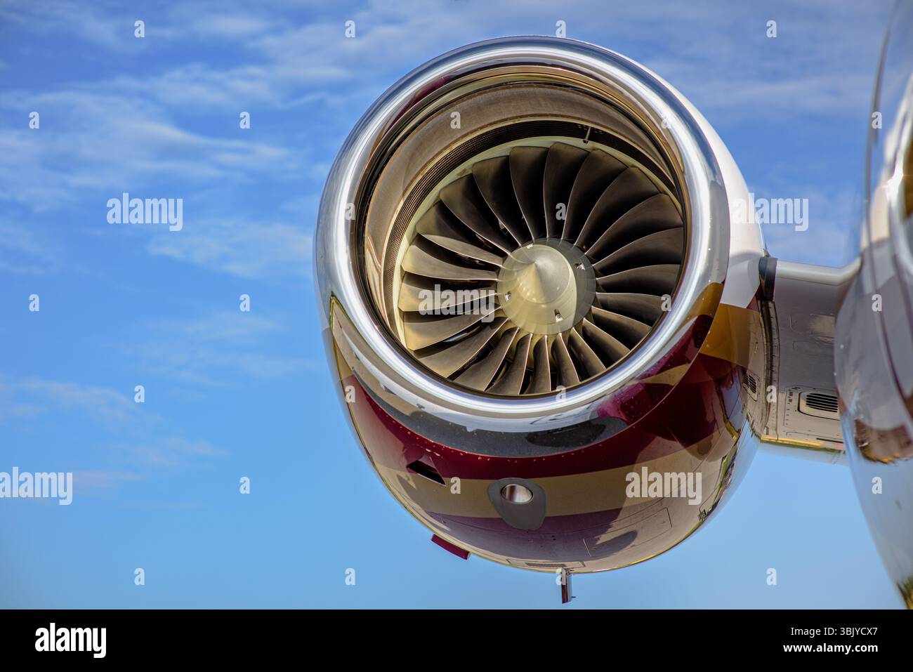 Primo piano del motore turbofan a bordo di un aereo business con livrea rossa e dorata, di fronte a un cielo azzurro. Pale della ventola e navicella chiaramente visibili. Foto Stock