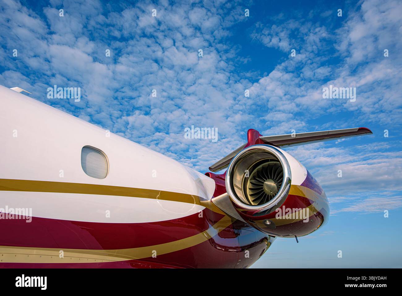 Vista posteriore di un lussuoso jet privato con una vivace livrea rossa e dorata su un cielo blu luminoso con nuvole. Coda, motore. Foto Stock