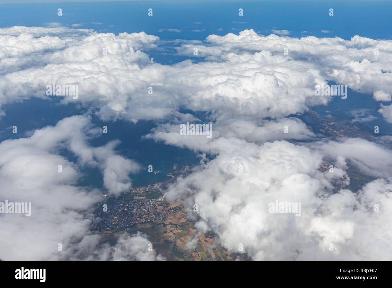 Una vista aerea mostra un paesaggio di nuvole che sovrastano la costa con l'oceano e la terra visibili, offrendo una prospettiva unica delle diverse caratteristiche della terra. Foto Stock
