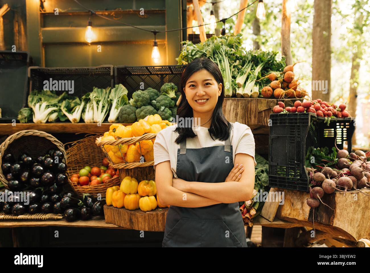 Ritratto di un dipendente sicuro del mercato all'aperto. Donna asiatica sorridente in un grembiule in piedi al suo stallo all'aperto. Foto Stock