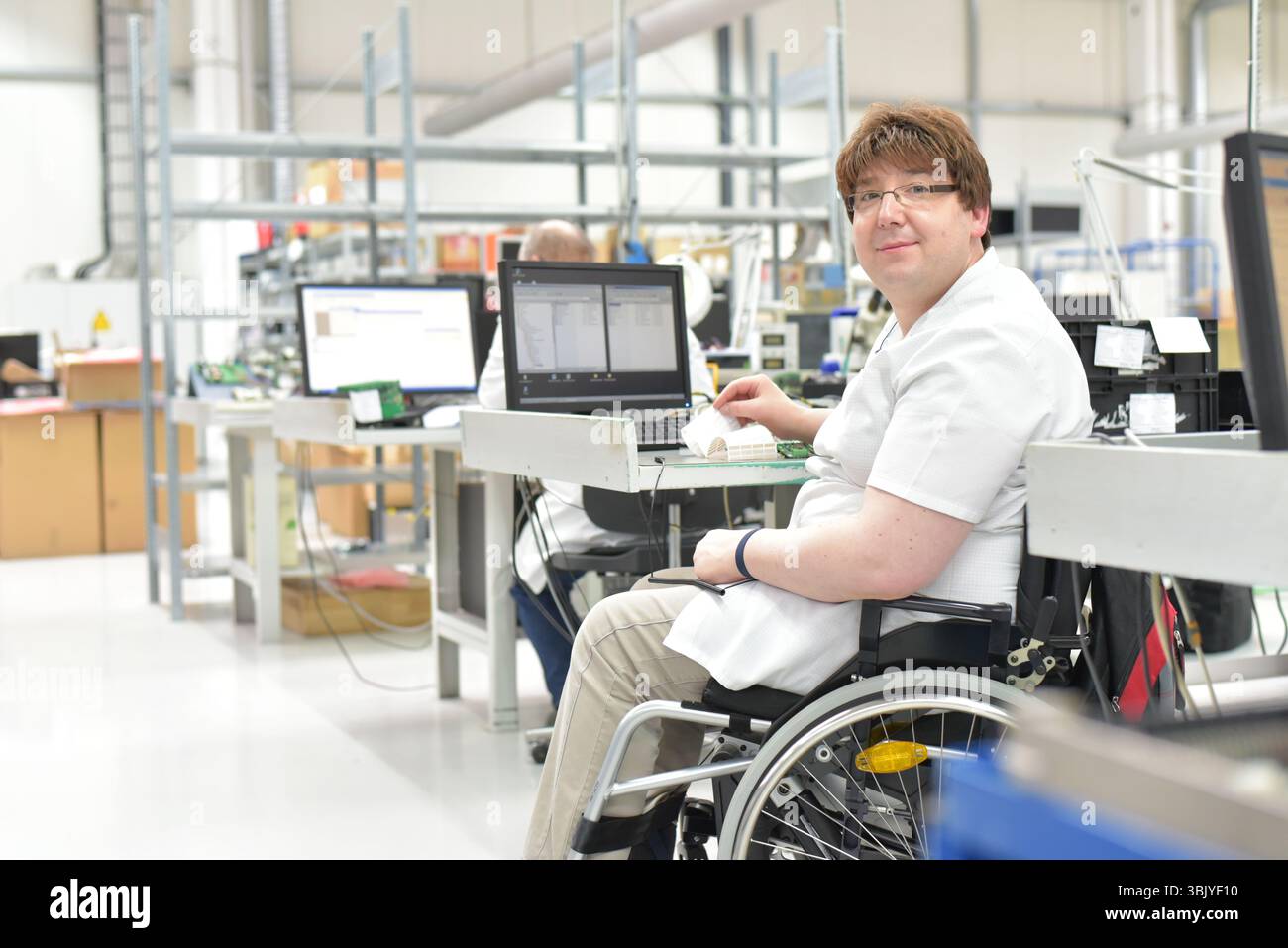 lavoratore portatore di handicap su una sedia a rotelle in un luogo di lavoro in una fabbrica di produzione e assemblaggio di componenti elettronici Foto Stock
