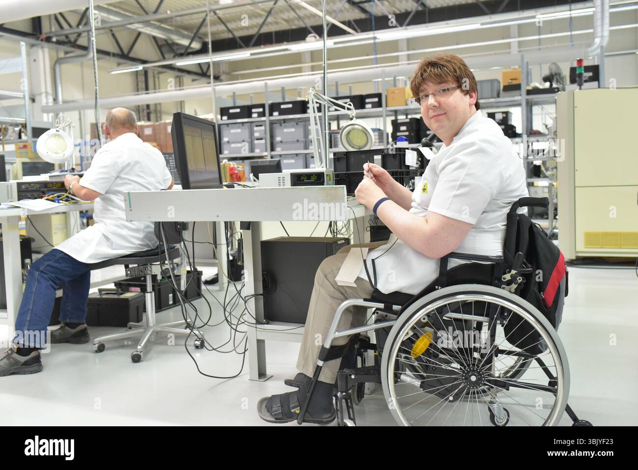 lavoratore portatore di handicap su una sedia a rotelle in un luogo di lavoro in una fabbrica di produzione e assemblaggio di componenti elettronici Foto Stock