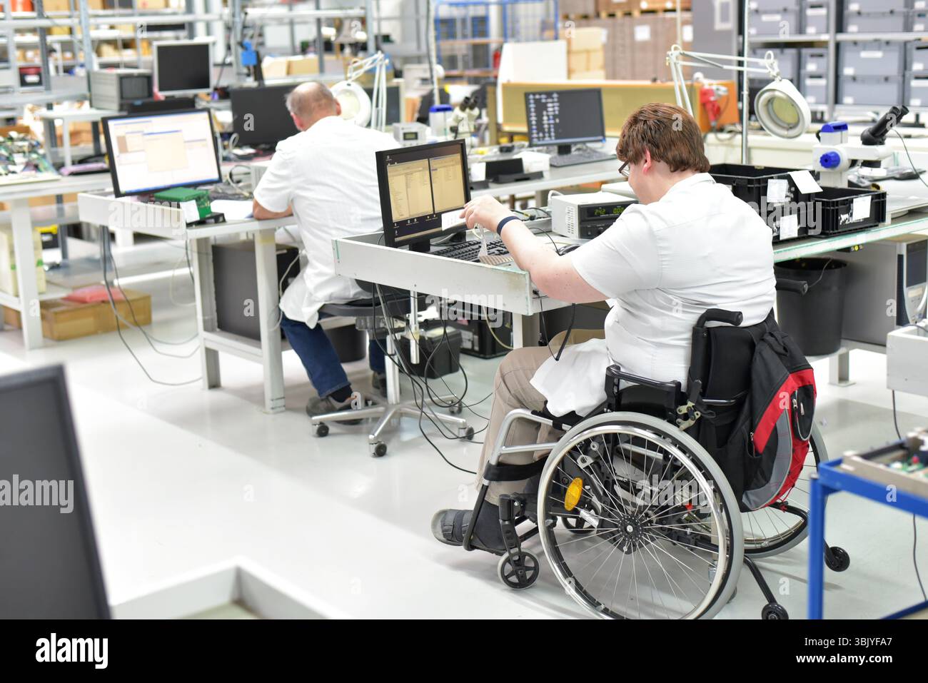 lavoratore portatore di handicap su una sedia a rotelle in un luogo di lavoro in una fabbrica di produzione e assemblaggio di componenti elettronici Foto Stock