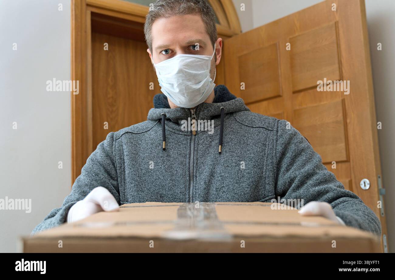 Il corriere in maschera medica e guanti consegna la confezione. Servizio di consegna pacchi. Foto Stock