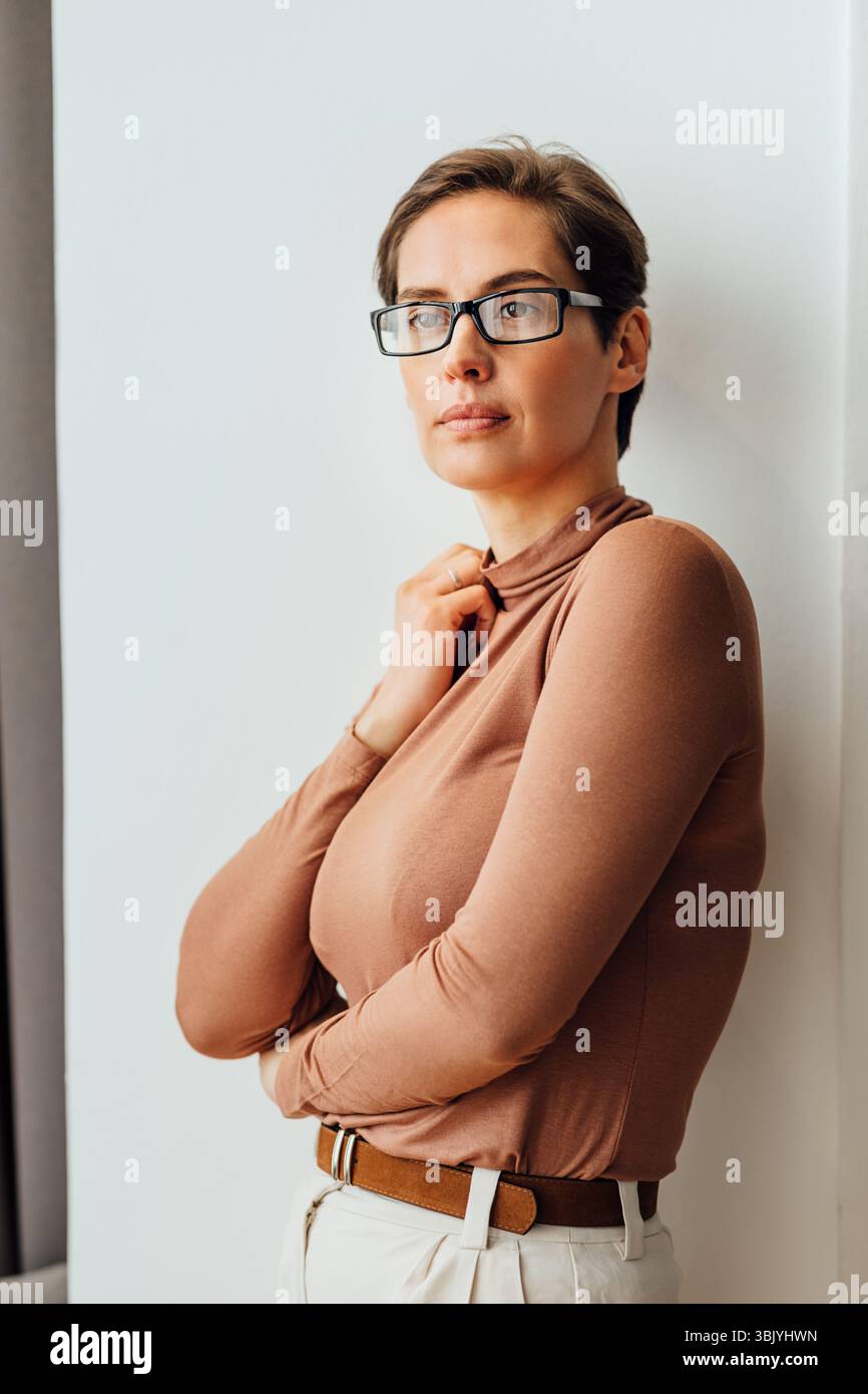 Ritratto di una donna d'affari in abbigliamento formale in piedi a parete. Occhiali da donna che indossano guardando lontano. Foto Stock