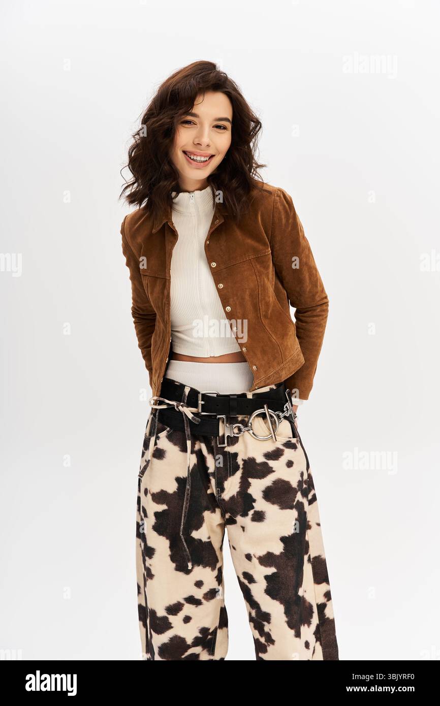 Una giovane donna con un sorriso giocoso modella un outfit alla moda con pantaloni con stampa mucca in uno studio. Foto Stock