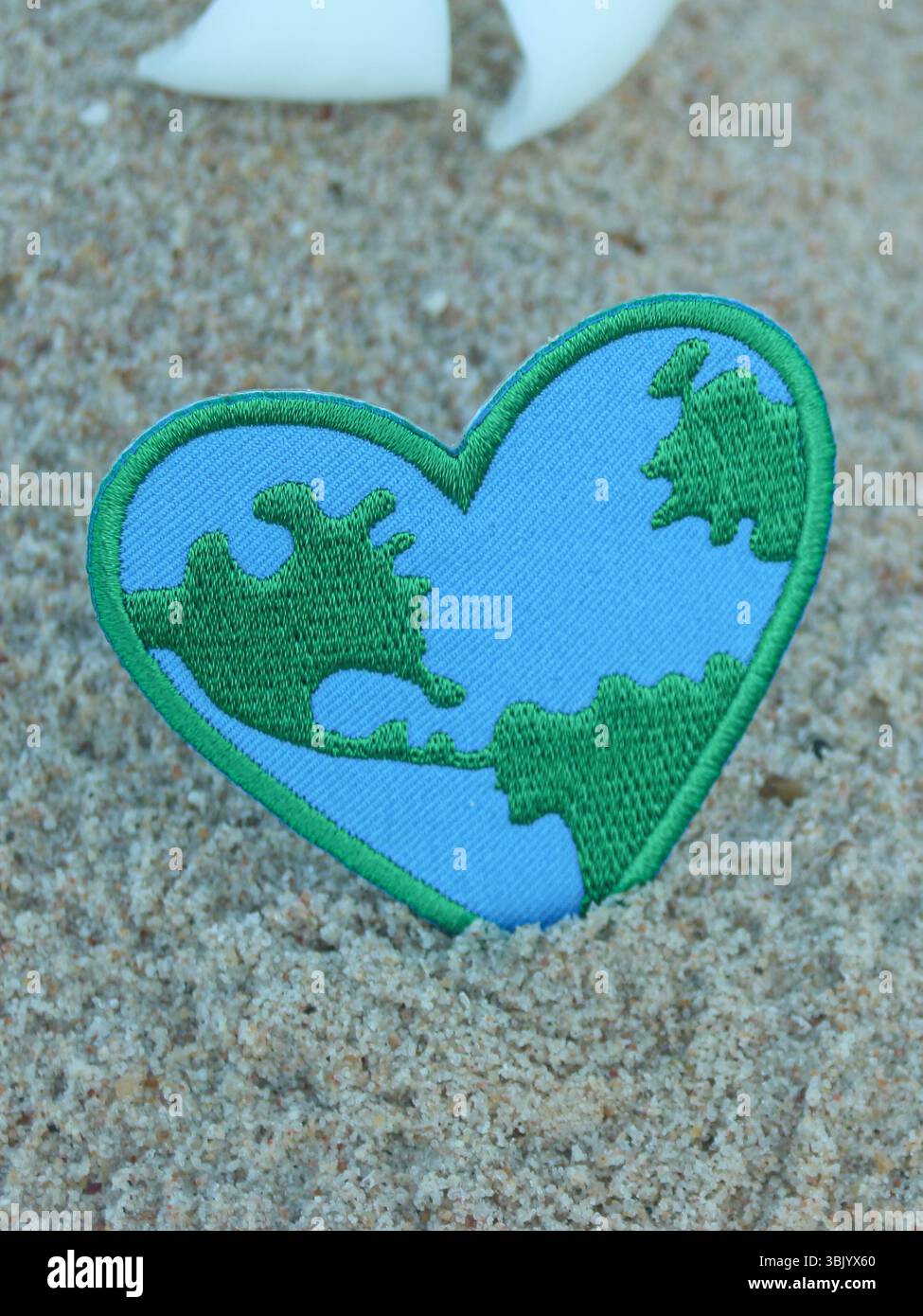 Cuore cucito a mano con motivo Terra sulla spiaggia di sabbia che simboleggia l'amore per la natura e la consapevolezza ambientale globale composizione verticale di luce naturale. Foto Stock