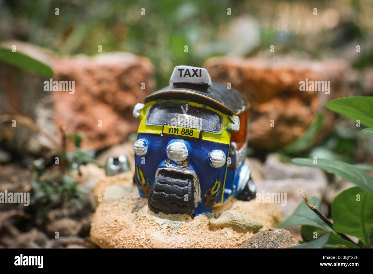 Primo piano di una colorata scultura in tuk-tuk tailandese in miniatura su rustica pietra marrone con sfondo morbido. Concetto di trasporto rurale in Thailandia d'epoca. Foto Stock