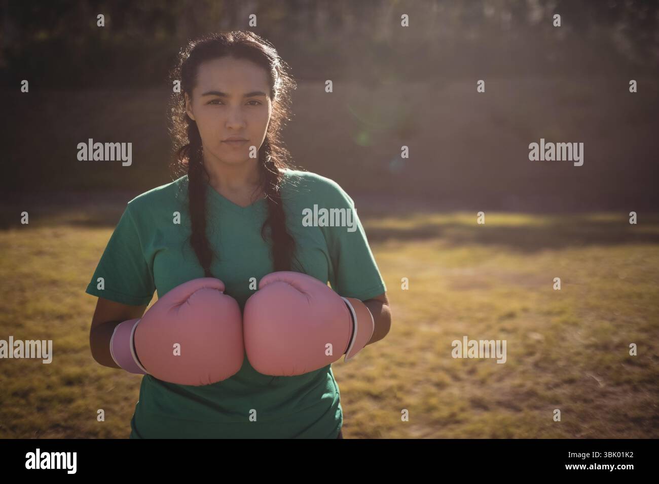 L'atleta indossa una camicia verde, regge guanti da boxe rosa in un campo illuminato dal sole con ombre lunghe Foto Stock