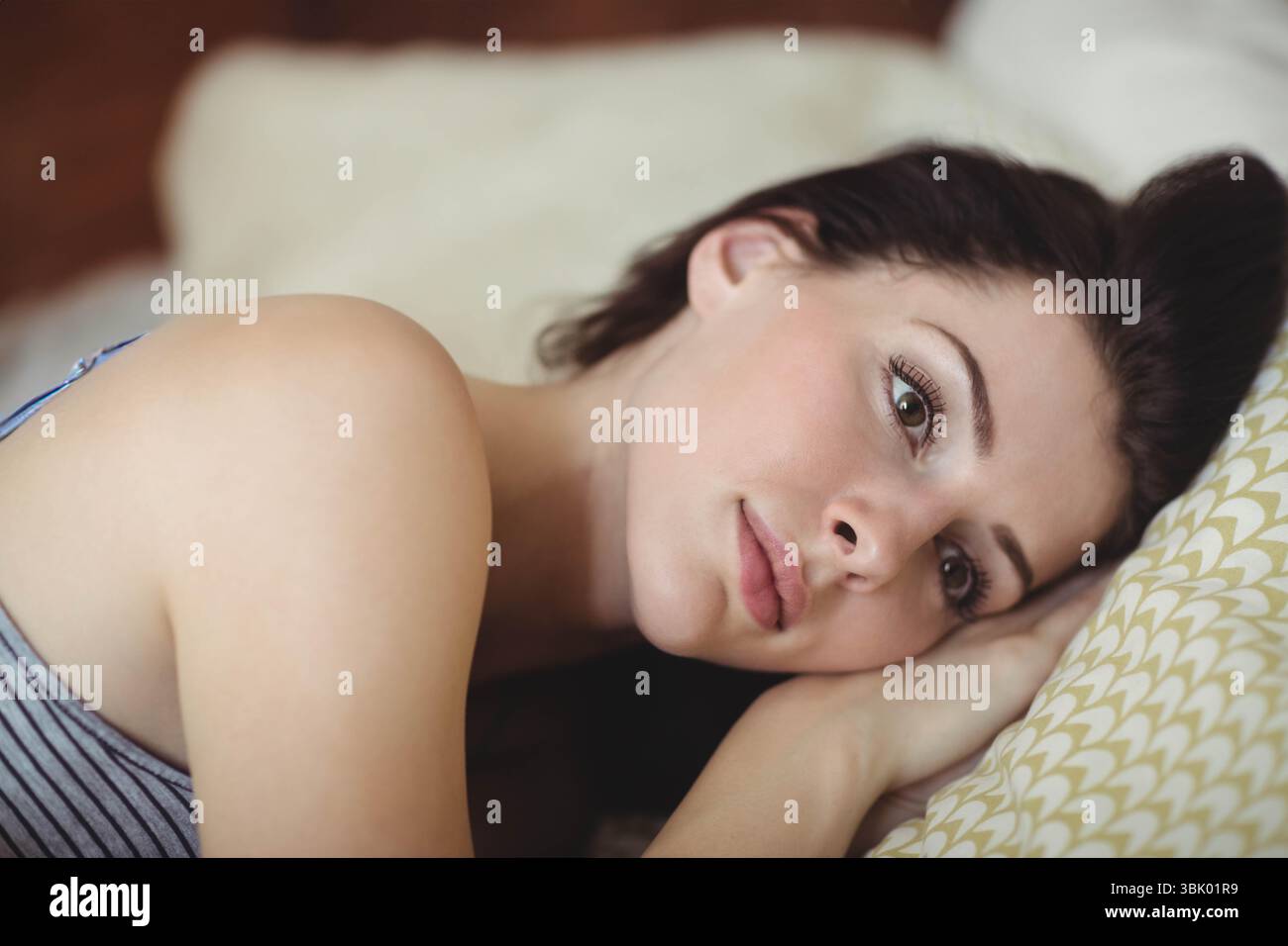 Donna sdraiata su un lato sul materasso in camera da letto con federa con motivi a foglia e morbide lenzuola Foto Stock