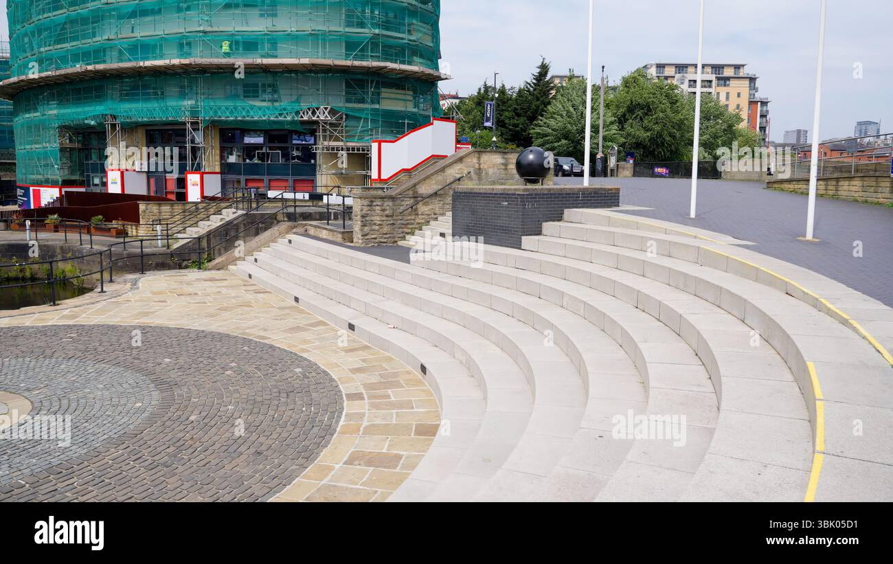 LEEDS, Regno Unito - 12 GIUGNO 2025 - gradini semicircolari di un anfiteatro all'aperto con pavimentazione in ciottoli vicino a un edificio in fase di ristrutturazione a Leeds, United Ki Foto Stock