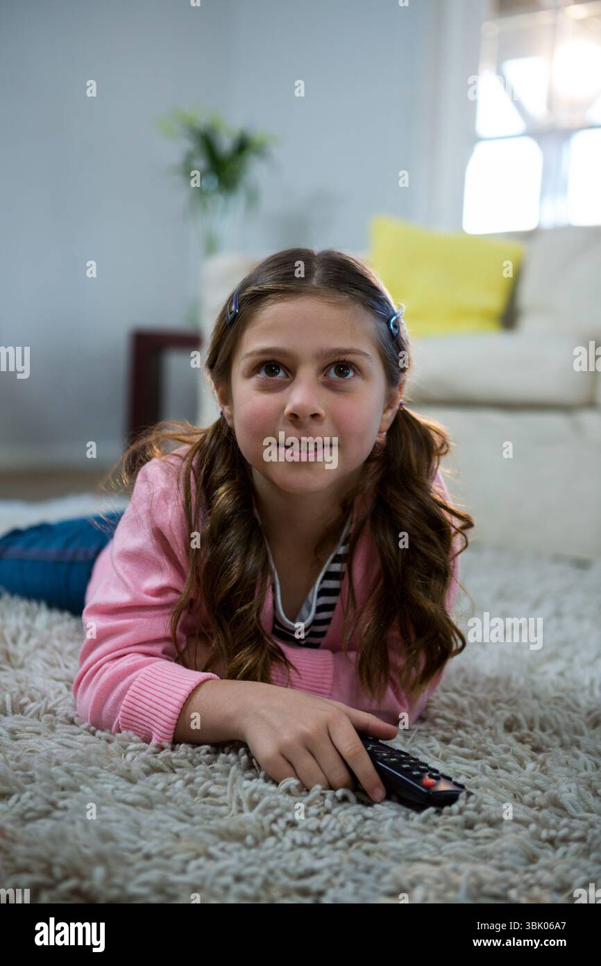 Telecomando TV appoggiato su morbido tappeto beige vicino al divano bianco, cuscino giallo sotto luce soffusa Foto Stock