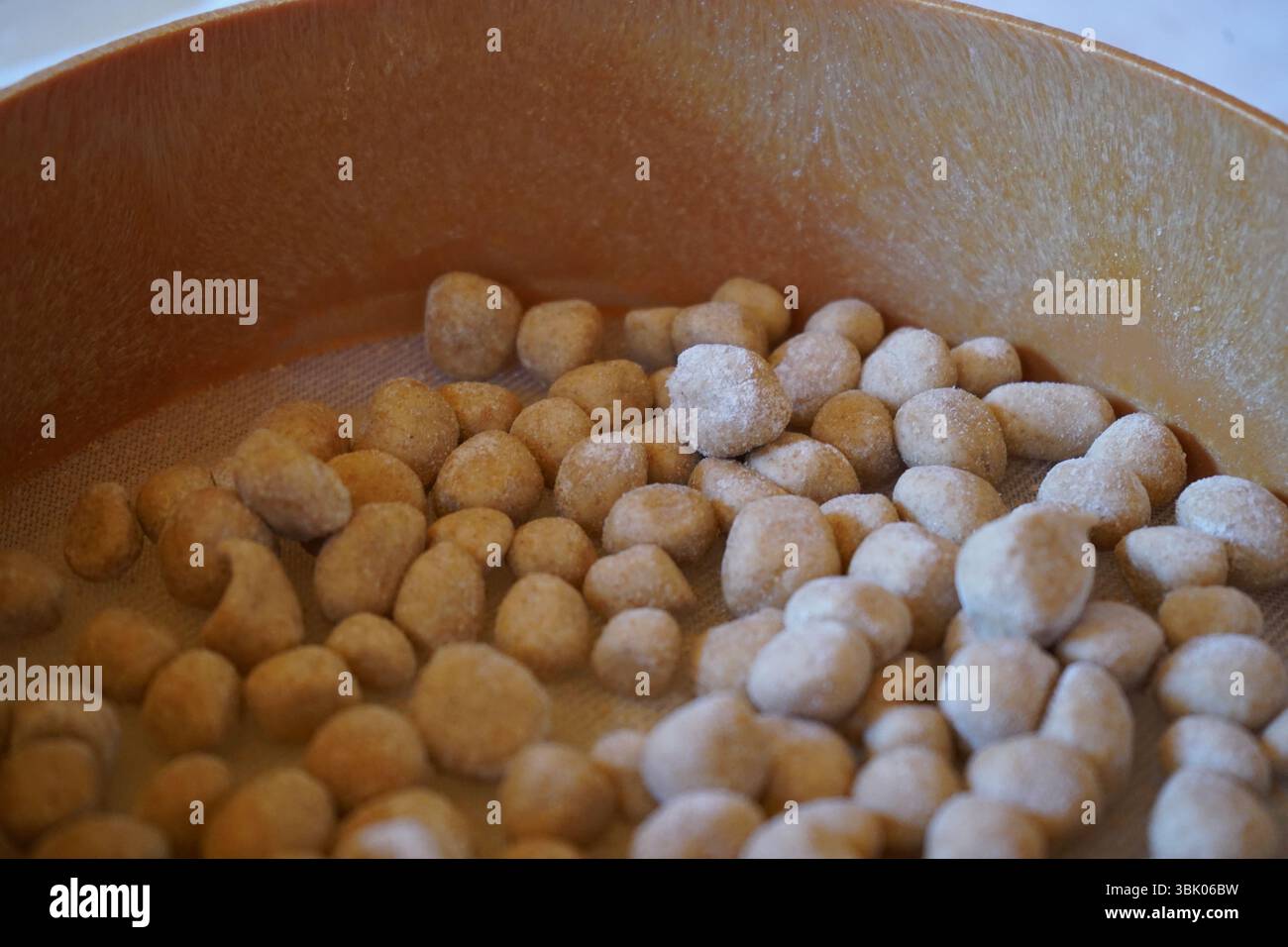 Primo piano di un setaccio rotondo in legno contenente piccole palline di impasto rotonde, la "topia" spolverata di farina, appoggiata su una superficie bianca. Cibo cretese. Foto Stock