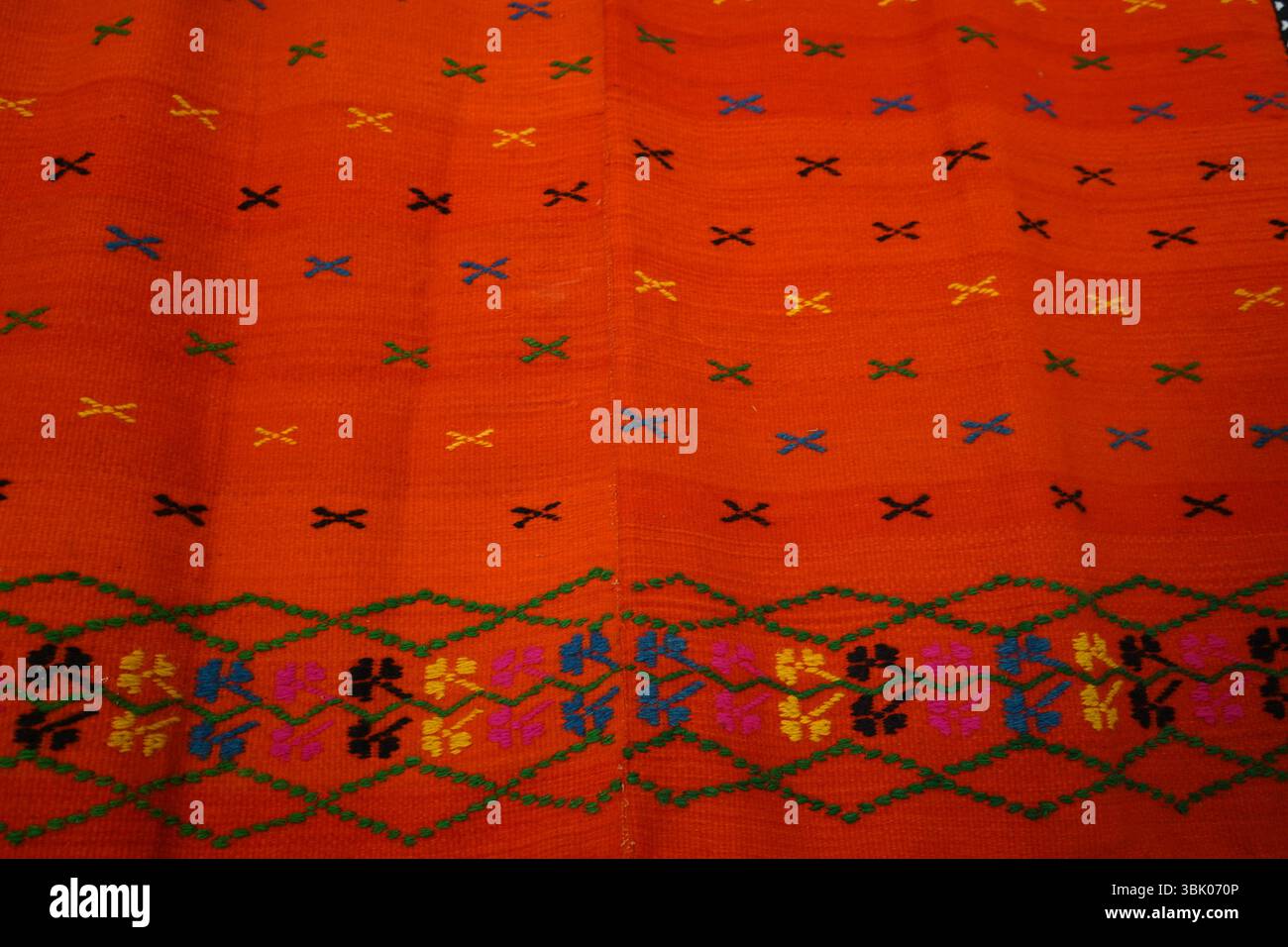 Coperta o tappeto tradizionale intrecciato a mano di Creta con vibrante sfondo arancione e ricami geometrici colorati. Splendido pezzo di texture popolare greca Foto Stock