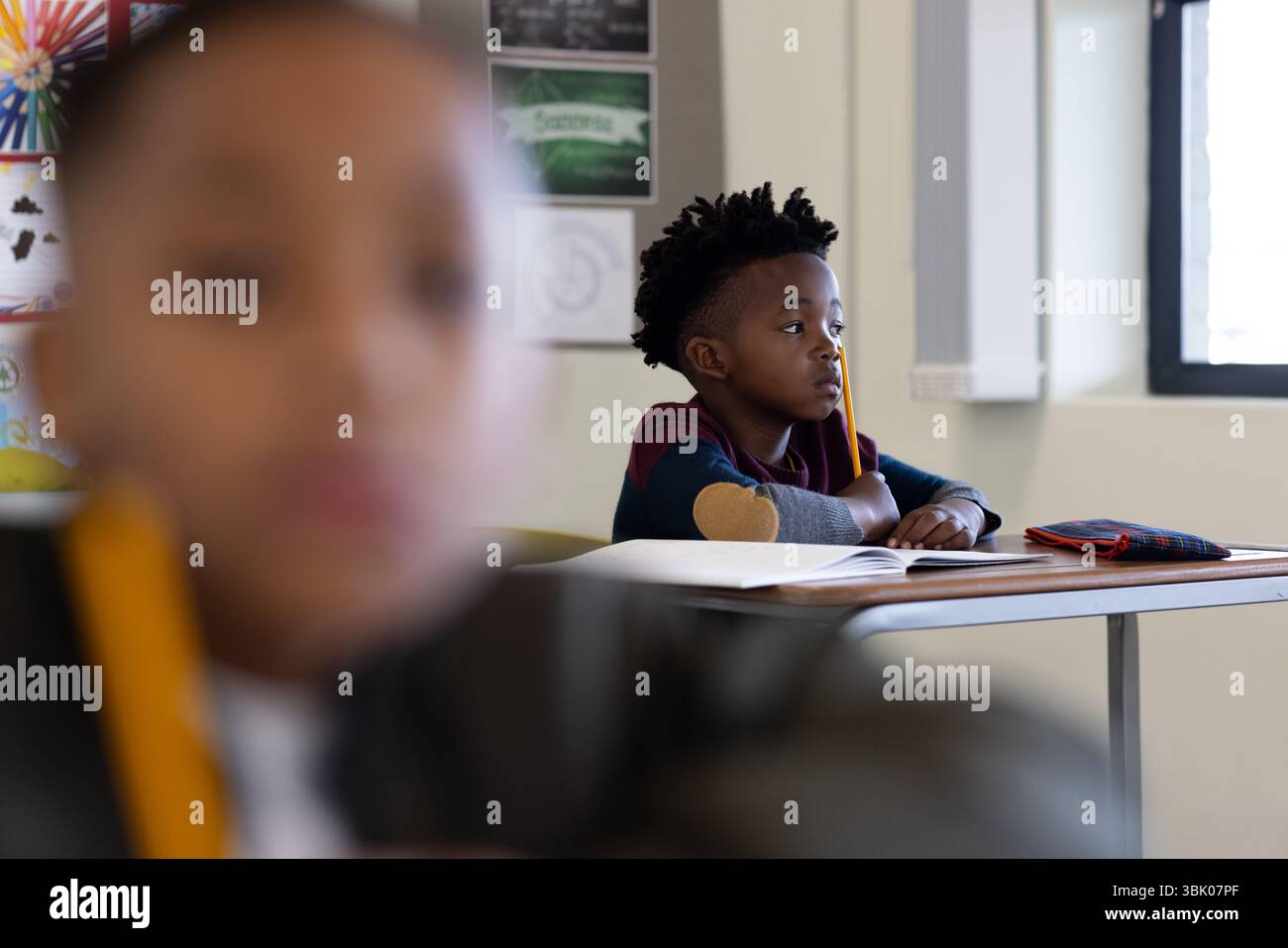 A scuola, ragazzo afroamericano concentrato che ascolta attentamente alla scrivania con matita e taccuino Foto Stock