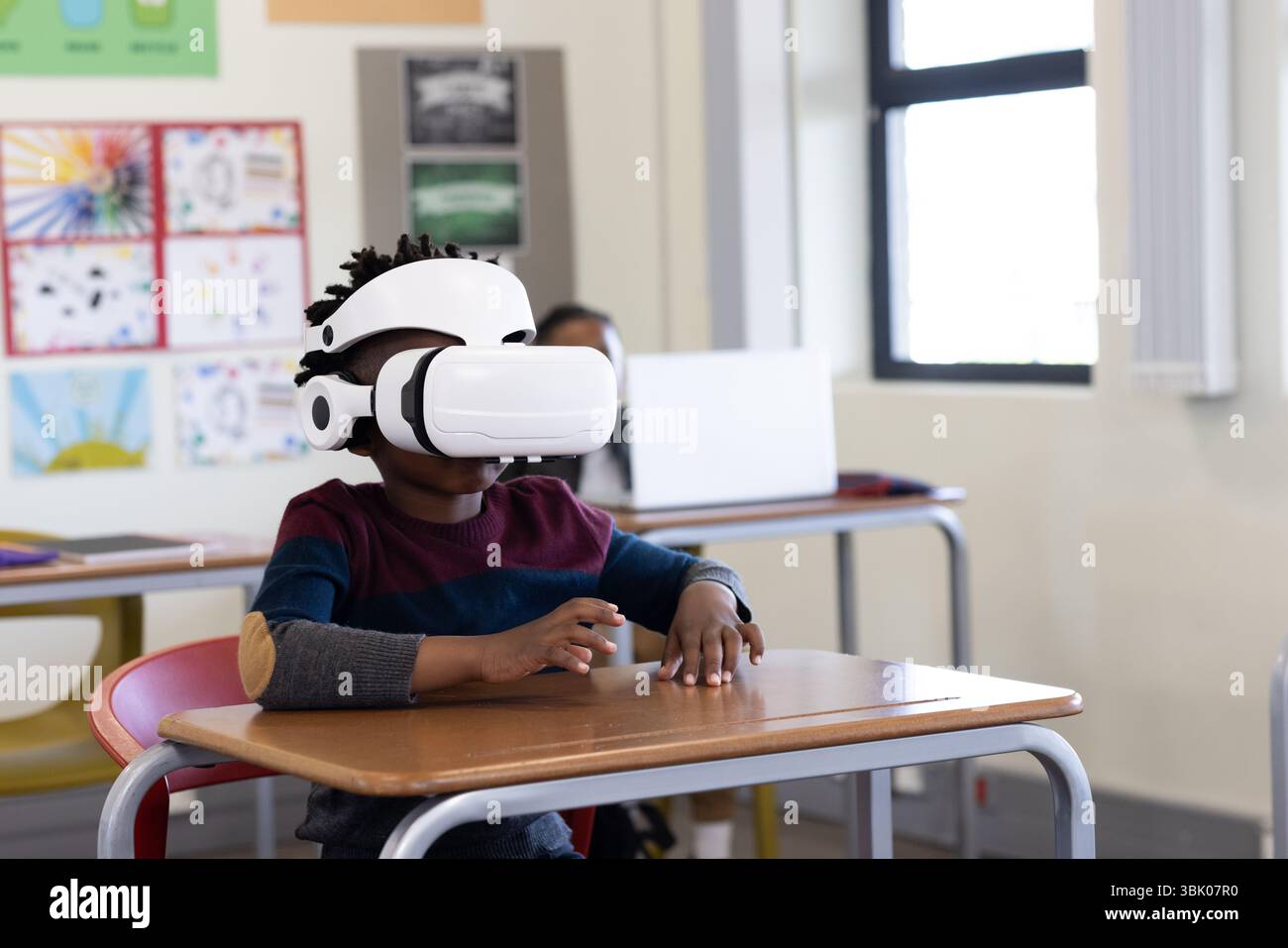 A scuola, ragazzo afroamericano che usa il visore VR alla scrivania, esplorando l'apprendimento virtuale Foto Stock