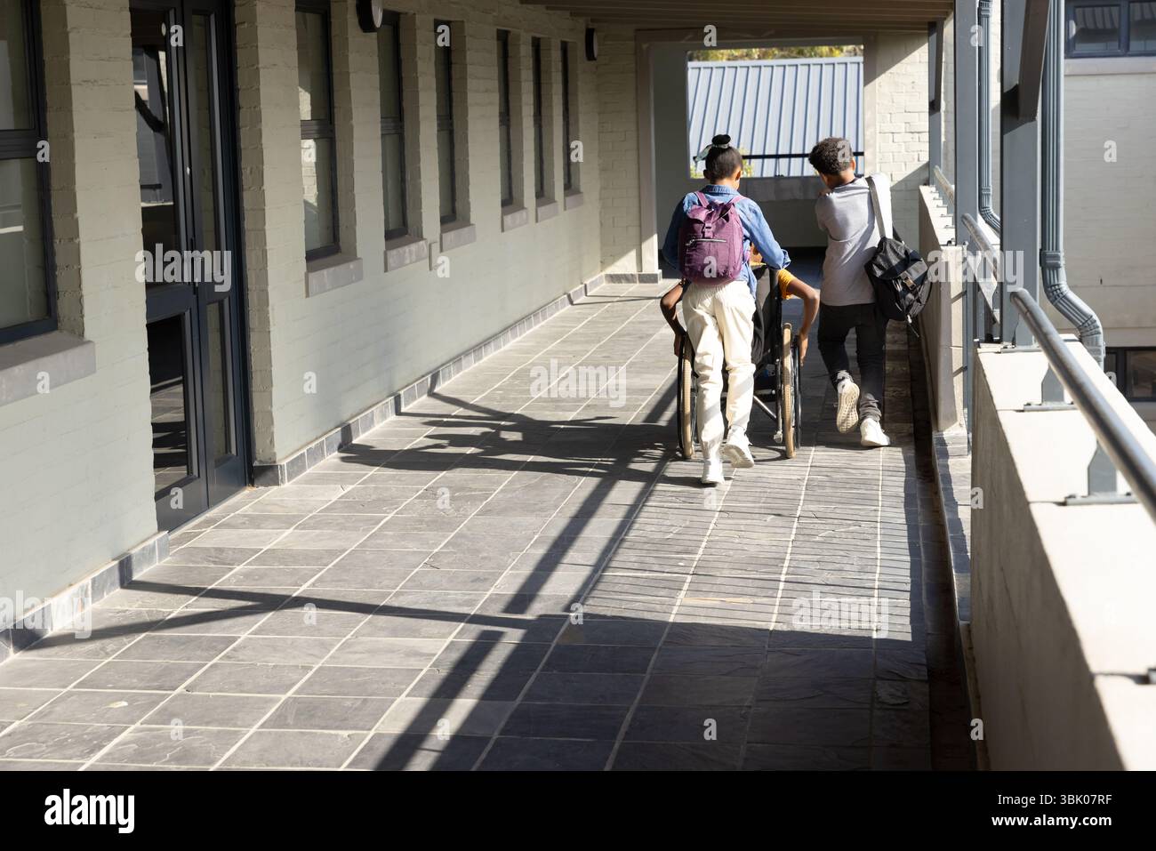 Camminando nel corridoio scolastico, diversi studenti con zaini, uno su sedia a rotelle Foto Stock