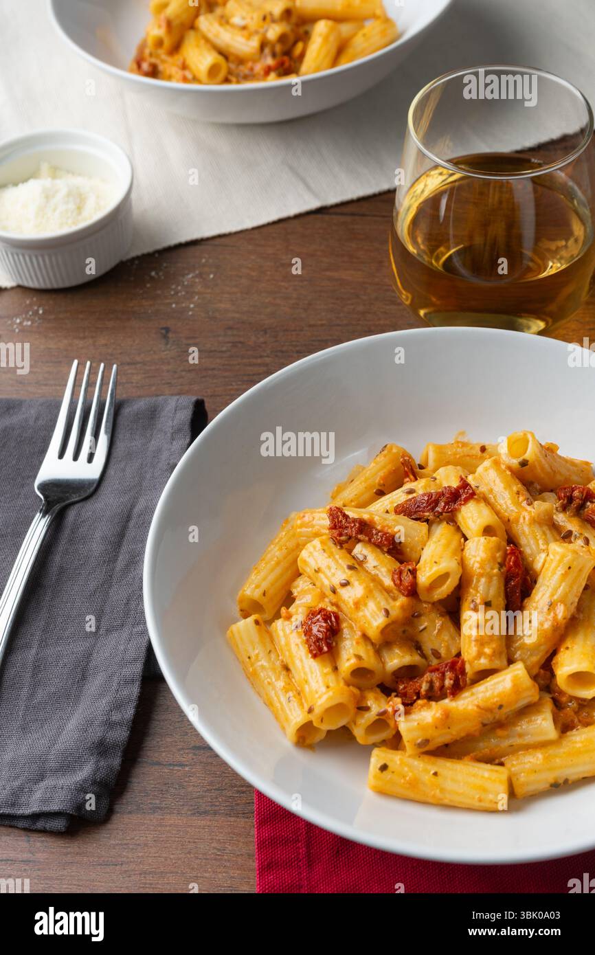 Pasta vegana con pomodoro secco servita su un piatto bianco profondo visto da un angolo di 45 gradi. Accanto al piatto si trova una forchetta con un tessuto grigio, Foto Stock
