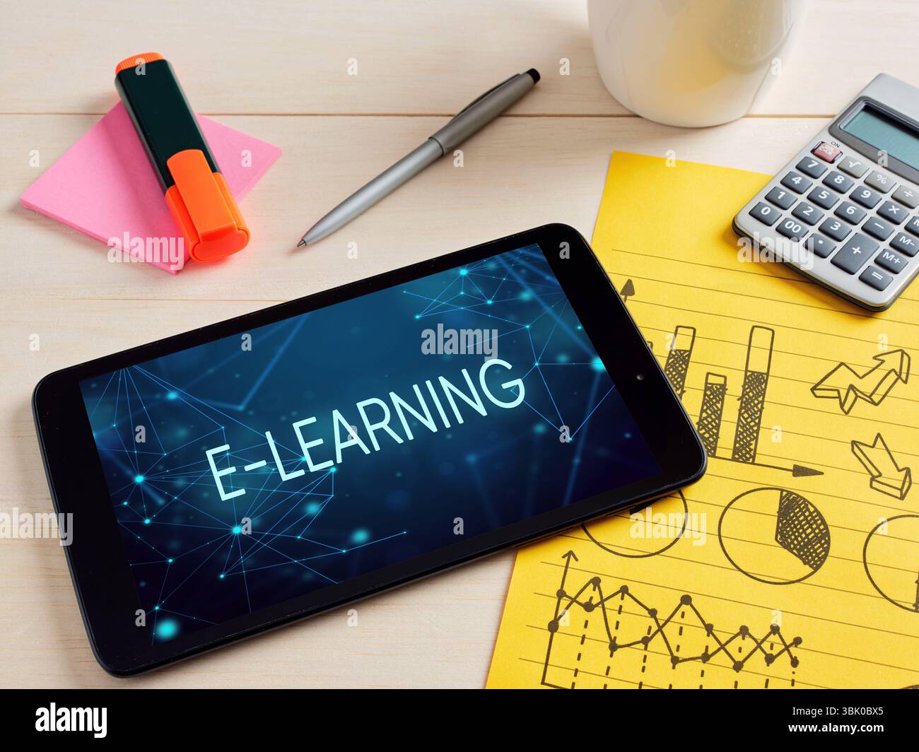 Tablet digitale che mostra un concetto di e-learning, appoggiato su una scrivania con forniture per ufficio e un blocco note con grafici e diagrammi. Foto Stock