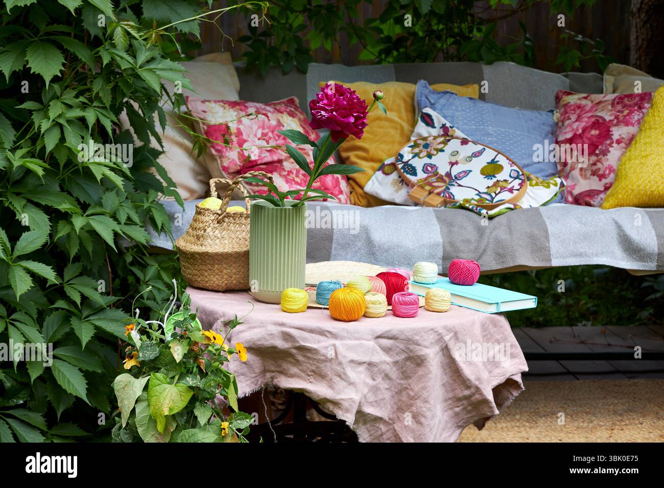 Un accogliente angolo esterno per la creatività in un giardino estivo: Un'altalena imbottita funge da posto rilassante per il ricamo, circondato da una vegetazione lussureggiante e. Foto Stock