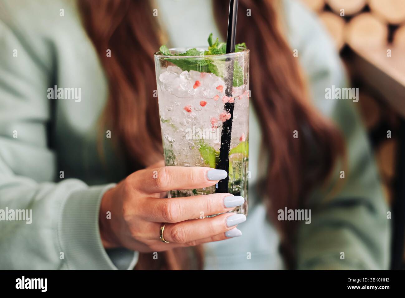 Cocktail mojito fresco in mano alla donna. Drink estivo con menta, ghiaccio e calce in vetro alto. Bevanda rinfrescante con cannuccia. Stile di vita all'aperto. Foto Stock