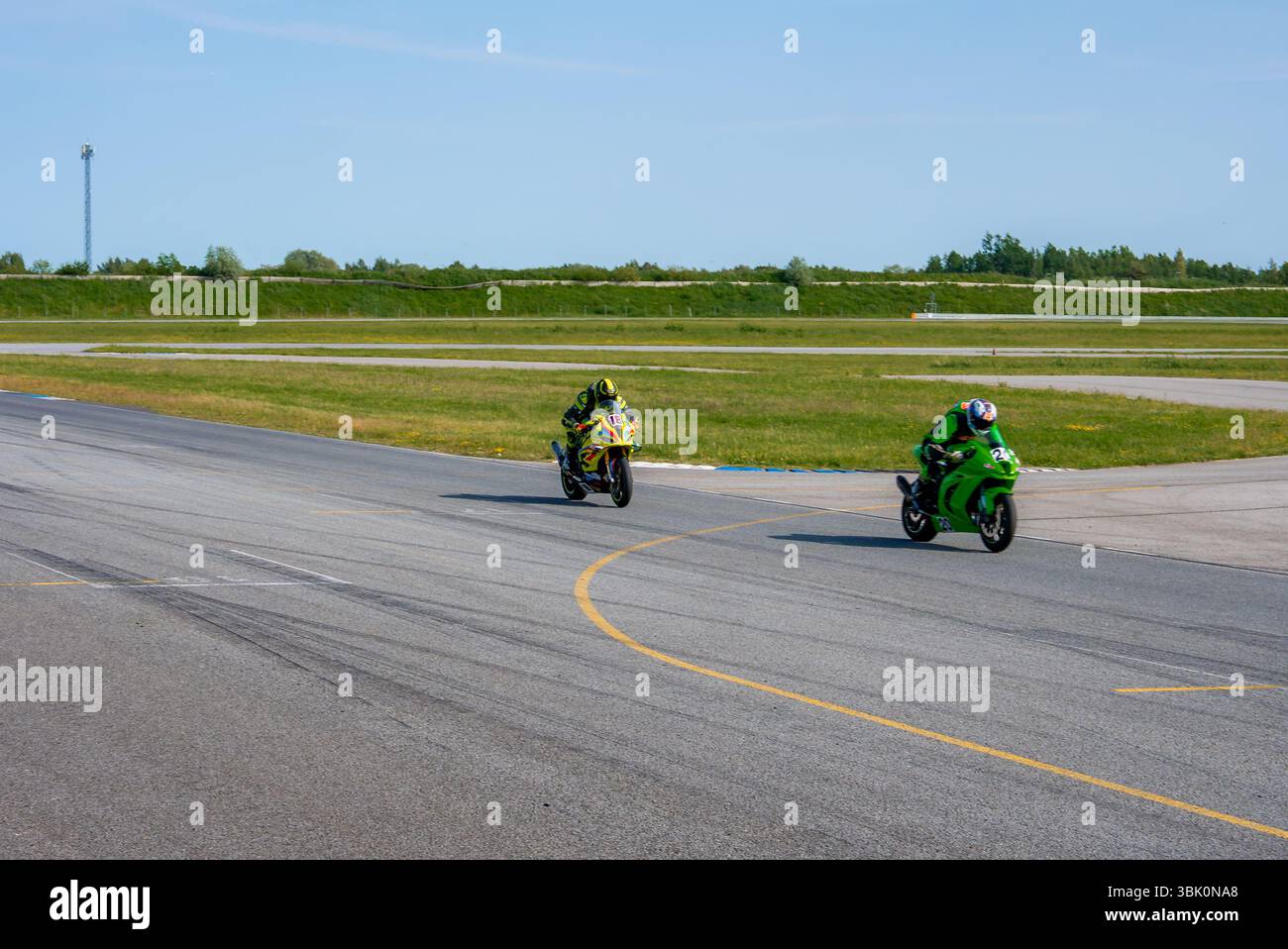 Due motociclisti corrono su una pista pavimentata sotto un cielo azzurro Foto Stock
