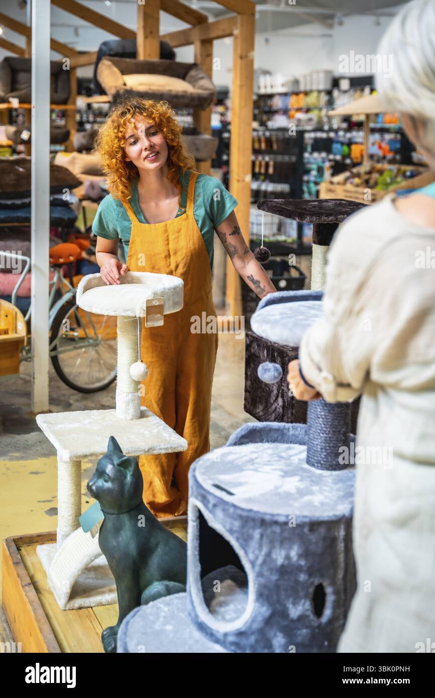 Venditore che interagisce con un cliente presentando vari post di graffiamento del gatto all'interno di un negozio di animali, evidenziando le opzioni e fornendo assistenza Foto Stock