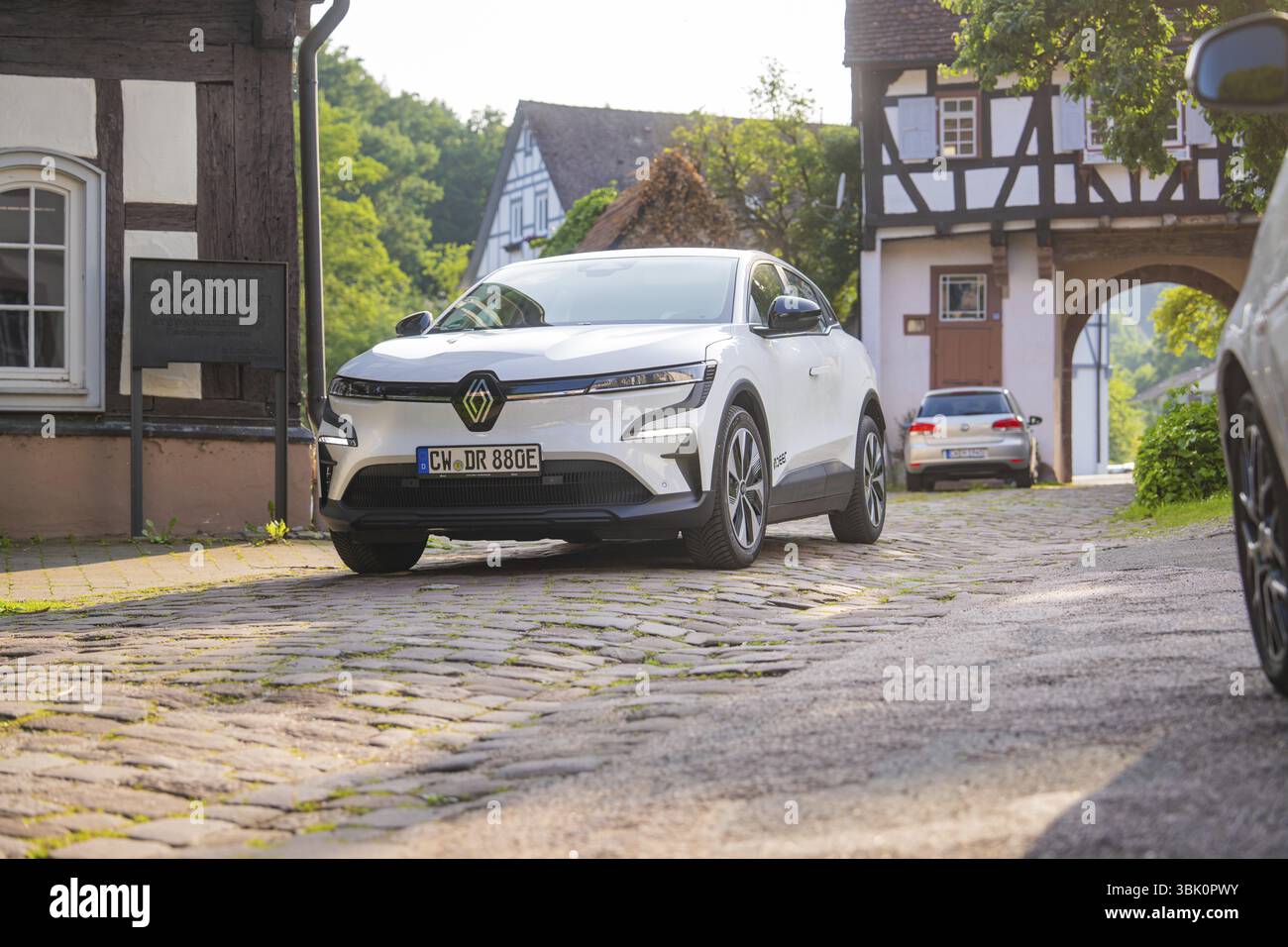 Auto bianca su una strada acciottolata in un pittoresco villaggio con case in legno, Renault Megane, Deer e Carsharing, auto elettrica, Calw, foresta Nera Foto Stock