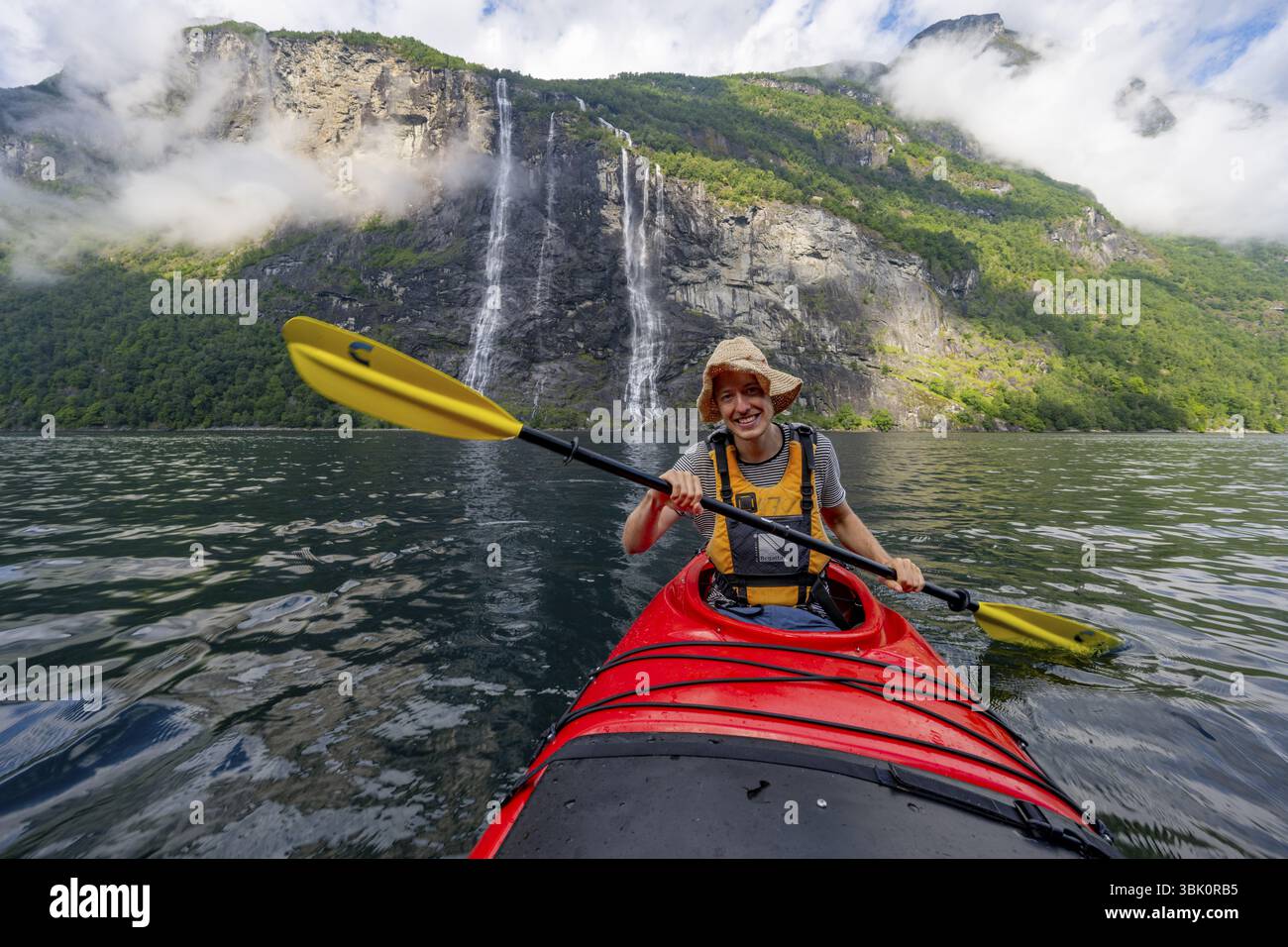 Gita in kayak sul Geirangerfjord presso la cascata The Seven Sisters, giovane pagaiando in kayak, suggestivo paesaggio dei fiordi, vicino a Geiranger e molto altro ancora Foto Stock