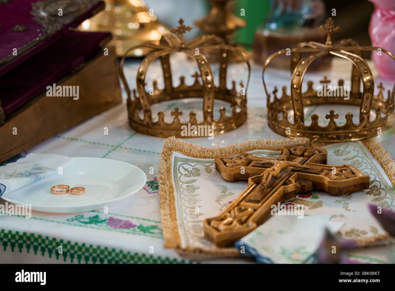 Primo piano di corone dorate ornate e di una croce con fedi nuziali, che rappresenta un sacramento del matrimonio cristiano ortodosso, che enfatizza la tradizione e il fait Foto Stock
