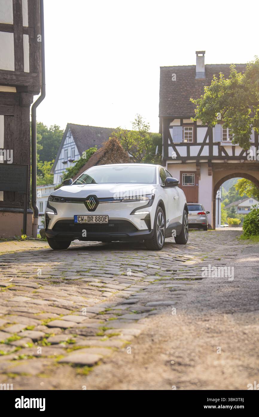 Un'auto bianca su una strada acciottolata in un villaggio con case a graticcio e un'atmosfera estiva, Renault Megane, Deer e- Carsharing, auto elettrica, GEC Foto Stock