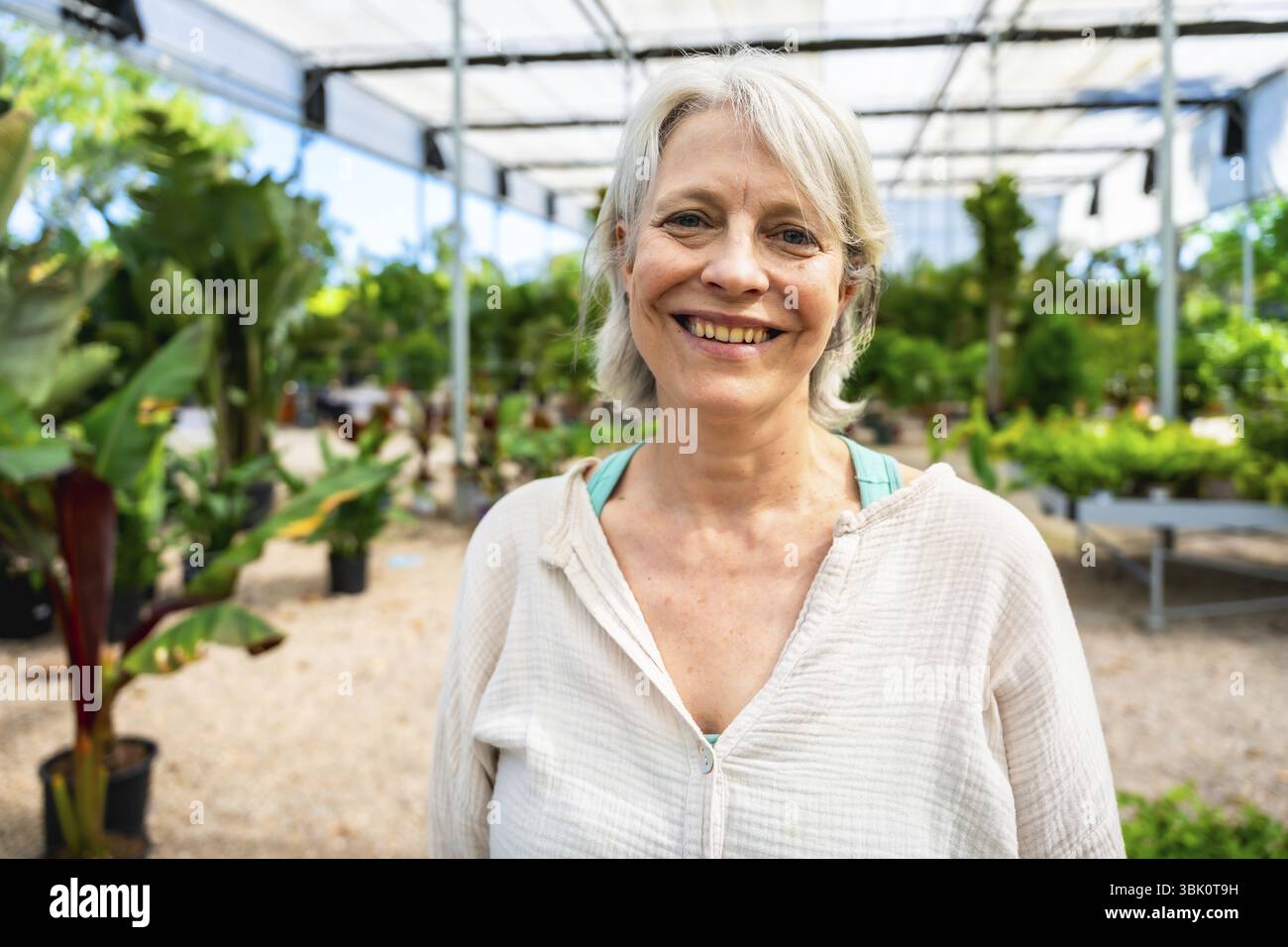 Ritratto di una donna allegra e matura che lavora gioiosamente in una serra, circondata da piante vivaci e lussureggianti e da una vegetazione fiorente Foto Stock