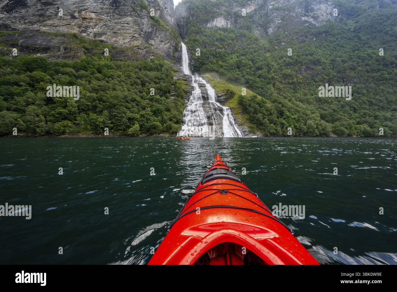 Gita in kayak sul Geirangerfjord presso la cascata Freier, punta di un kayak rosso nel fiordo, suggestivo paesaggio del fiordo, vista in prima persona, vicino a Geiran Foto Stock