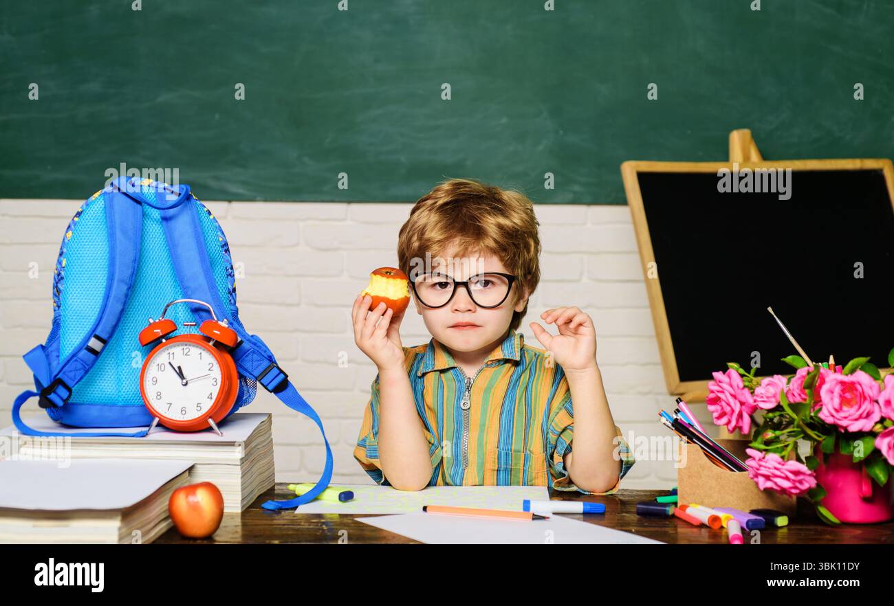 Ora di pranzo. Uno studente carino e serio seduto a tavola e mangiando mele in classe. Pausa scolastica. Cibo delizioso per pranzo. Cibo sano e gustoso per i bambini Foto Stock