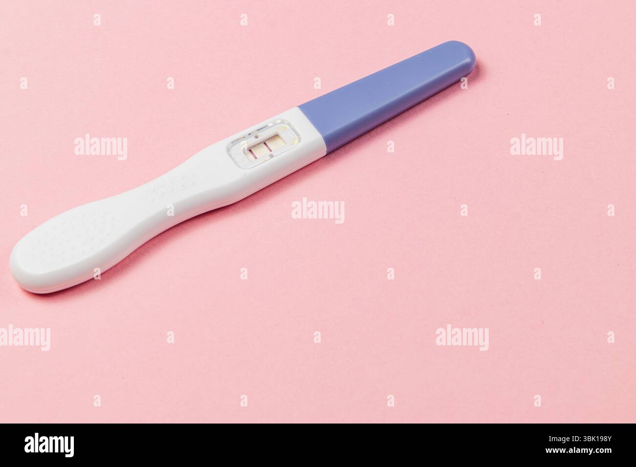 Un test di gravidanza visualizza due righe che indicano un risultato positivo. Il test viene posizionato su uno sfondo rosa tenue, evidenziandone le caratteristiche. Foto Stock
