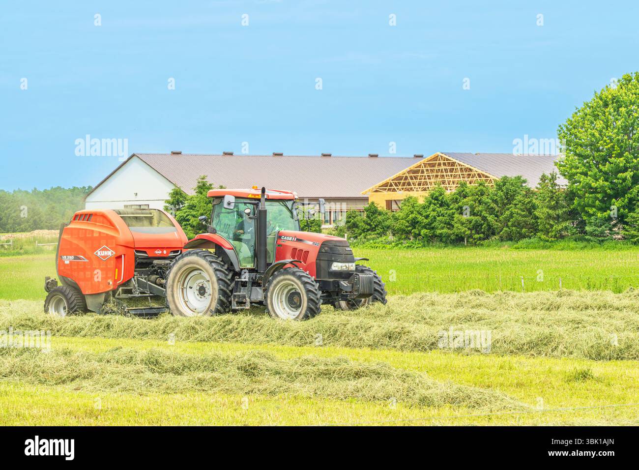 Agricoltore che traina rotopresse dietro il trattore in un campo vicino a Exeter Ontario Canada. Un buon cropis di fieno è importante per sostenere il bestiame durante l'inverno del mont Foto Stock
