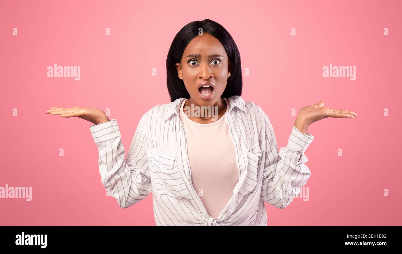 Infastidita donna afroamericana gesturing non SO, shrugging le spalle su sfondo rosa studio Foto Stock