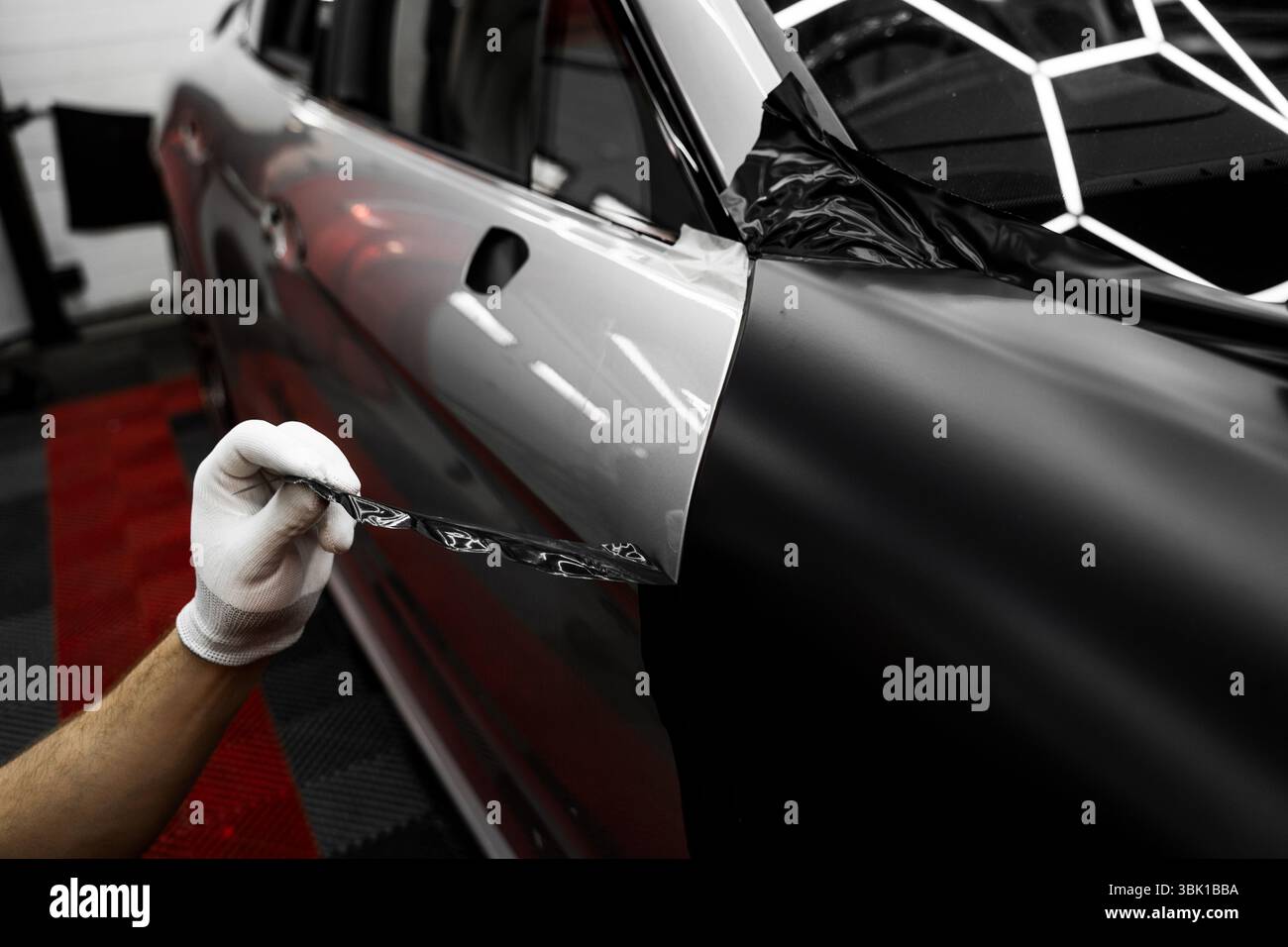 Rivestimento in vinile per auto a pannello intero. L'installazione di un involucro in vinile su larga scala trasforma l'esterno del veicolo con una pellicola nera opaca. Modifiche all'applicazione di avvolgimento per auto Foto Stock