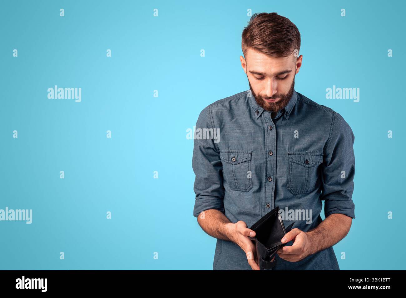 Povertà e disoccupazione. Disperato giovane uomo che mostra portafoglio vuoto senza soldi su sfondo blu studio Foto Stock