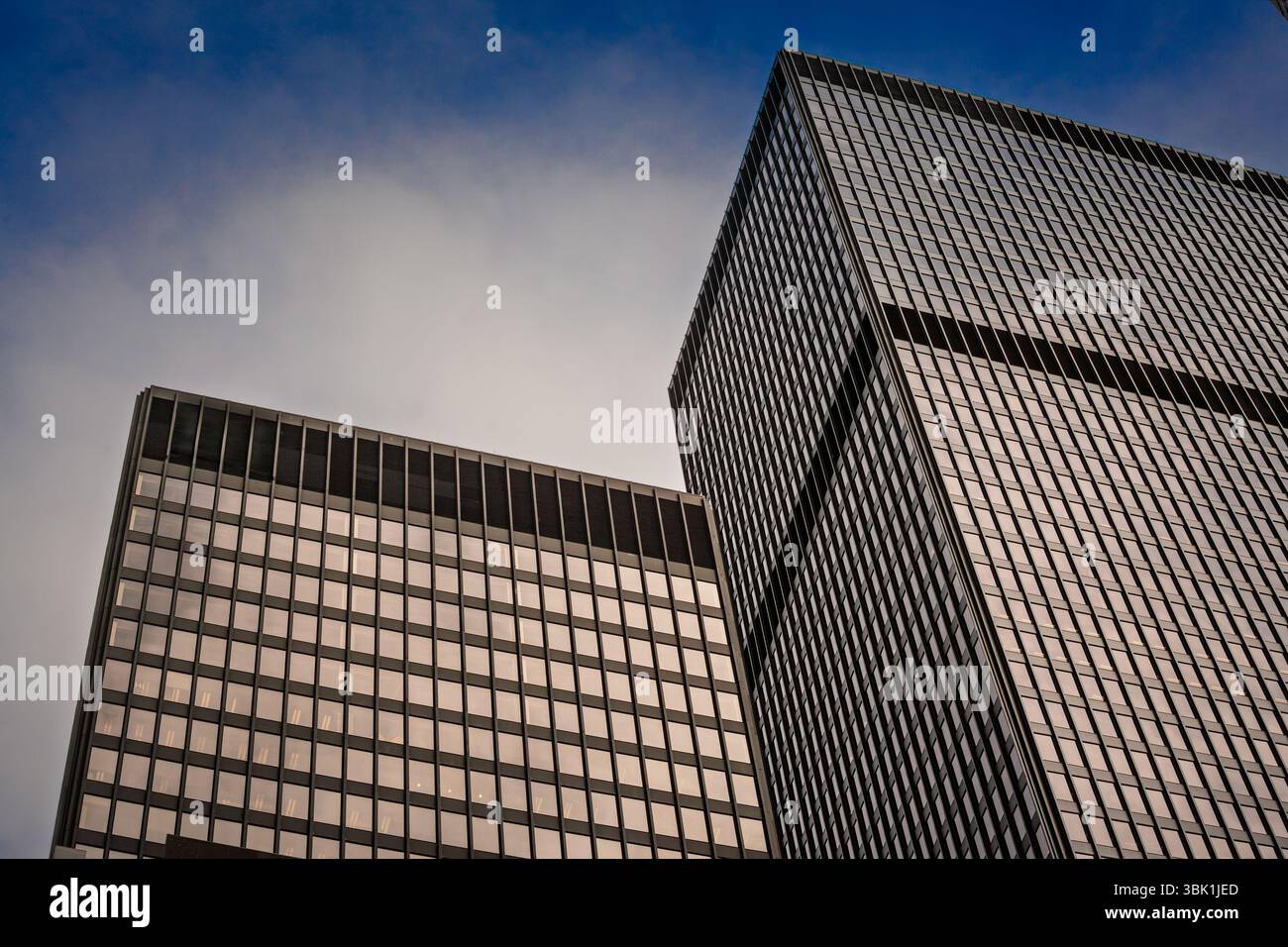 La vista verso l'alto di due torri nere in vetro e acciaio nel CBD del Nord America mostra facciate a griglia minimaliste che catturano la luce del crepuscolo e lo sgombero Foto Stock