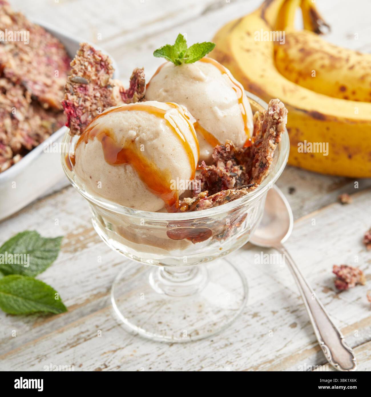 Cucchiai di bella crema di banana condita con salsa al caramello e briciole di biscotti: Un dessert surgelato vegano, dolce e cremoso, perfetto per l'estate. Foto Stock